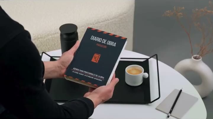 El Cuaderno DDO en la mano, tapa azul marino con la franja de aviso naranja.